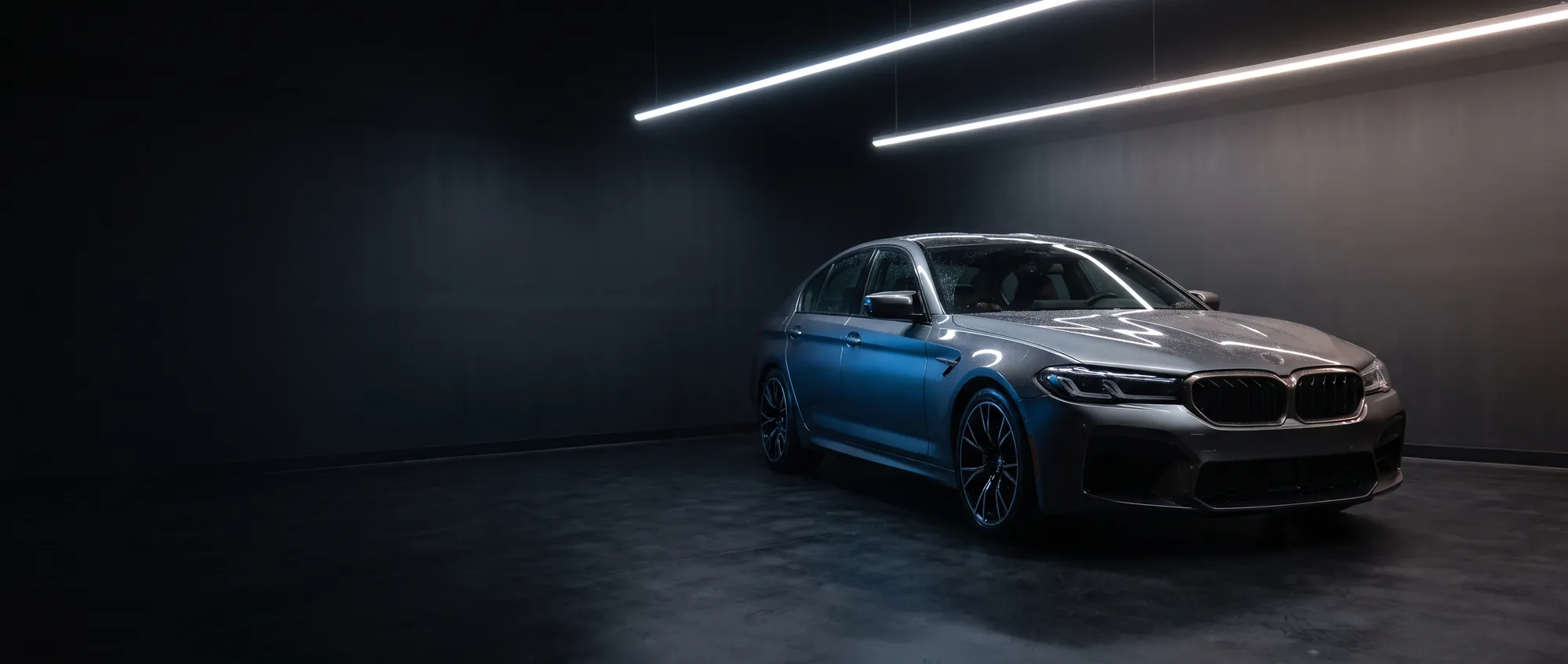 A dark performance sedan under linear studio lighting in the Gusheshe Garage installation bay.
